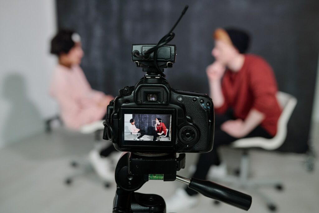 Screen of digital video camera with two vloggers sitting on chairs and talking